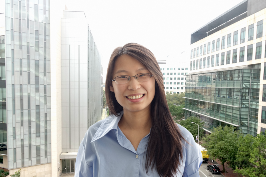 MIT postdoc Miaomiao Zhang stands in front of a window overlooking Main Street in Cambridge, Mass. Tall glass buildings are in the background.