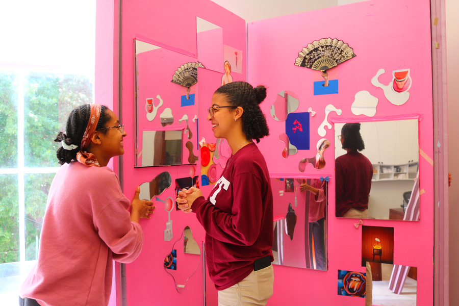 Two students laugh together against the bright pink backdrop festooned with whimsical decorations