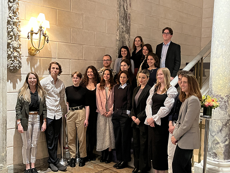 17 people pose for a picture in front of a staircase.