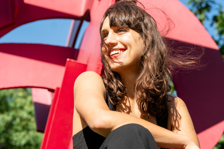 Jaye smiles while sitting down, with a red sculpture in background.