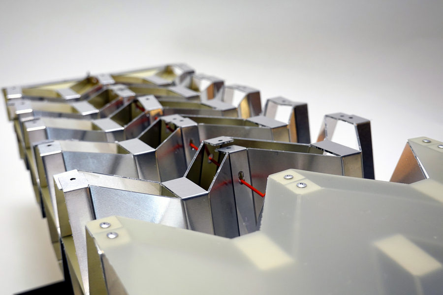 Close-up of an aluminum object shows a red chord that connects the modular pieces.