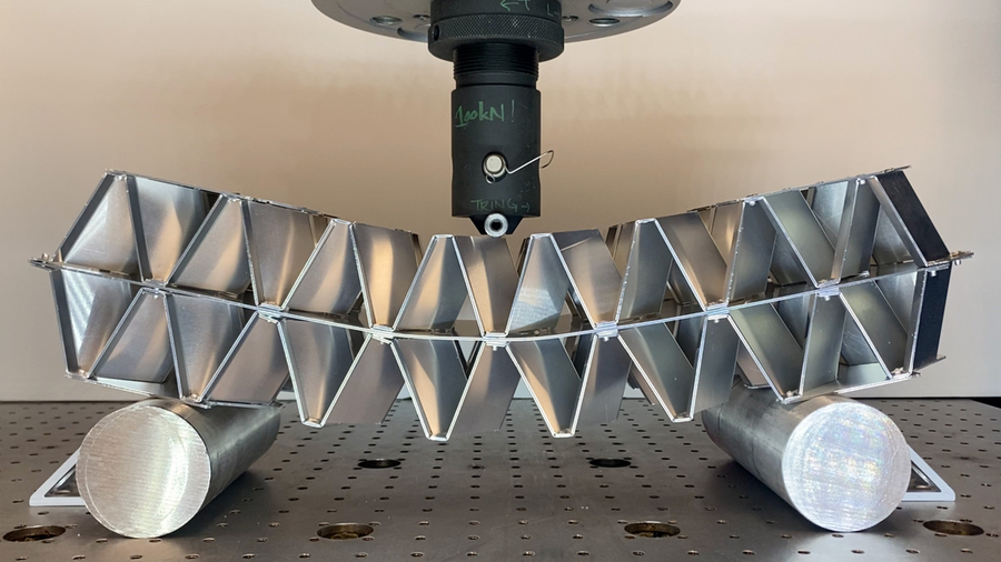 A long modular aluminum object is put under stress as a machine pushes down on the middle of it.