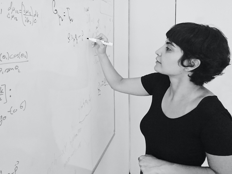Black-and-white photo of Leila Mirzagholi standing at a whiteboard, writing equations.