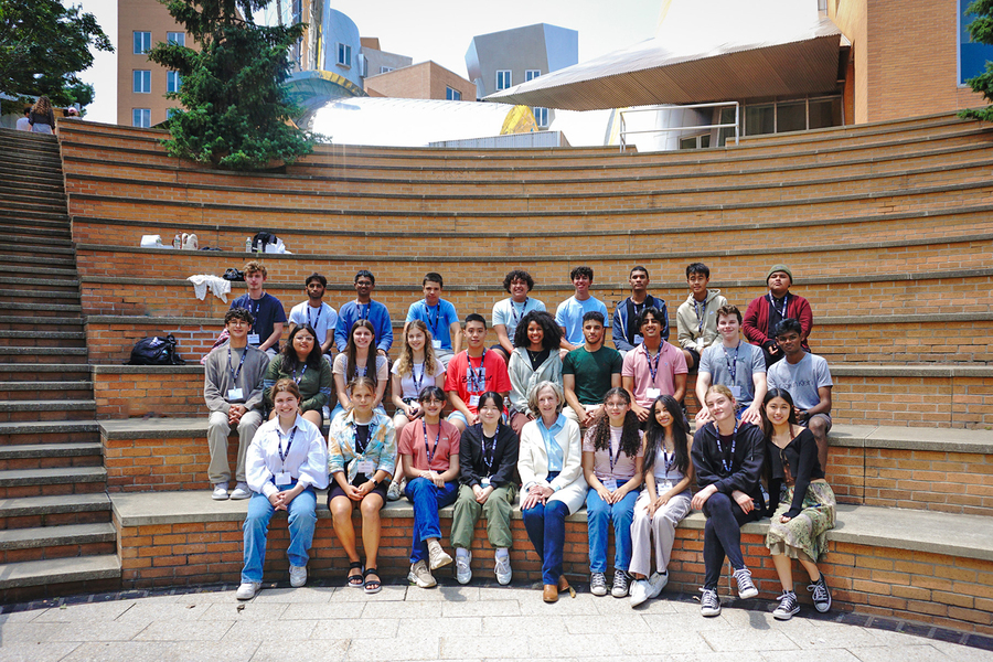 27 high school students sit in three rows along with Susan Hockfield in MIT's outdoor amphitheater