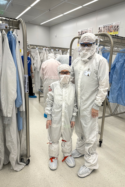 An adult with his arm around a child; both are wearing full-body, protective "bunny suits."