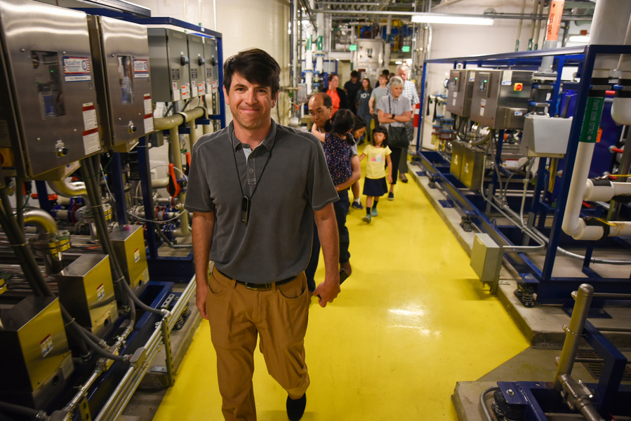 Nicholas Menounos leads a group of adults and children down a hallway filled with pumps and machines.