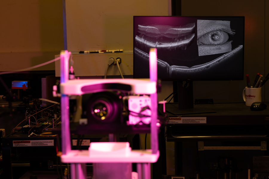 The chin rest used by a patient undergoing an optical scan is lit in pink in the foreground; in the background, a high-resolution image of a retina is shown. 