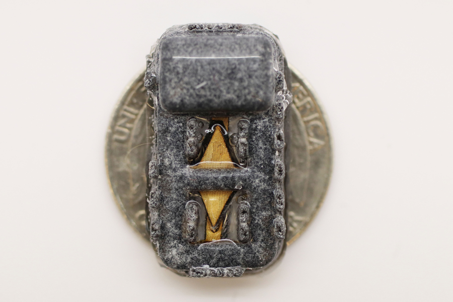 The tiny device fits on a quarter. The diamond-shaped piece of material is visible, but the rest of the device is covered in gray fibers.