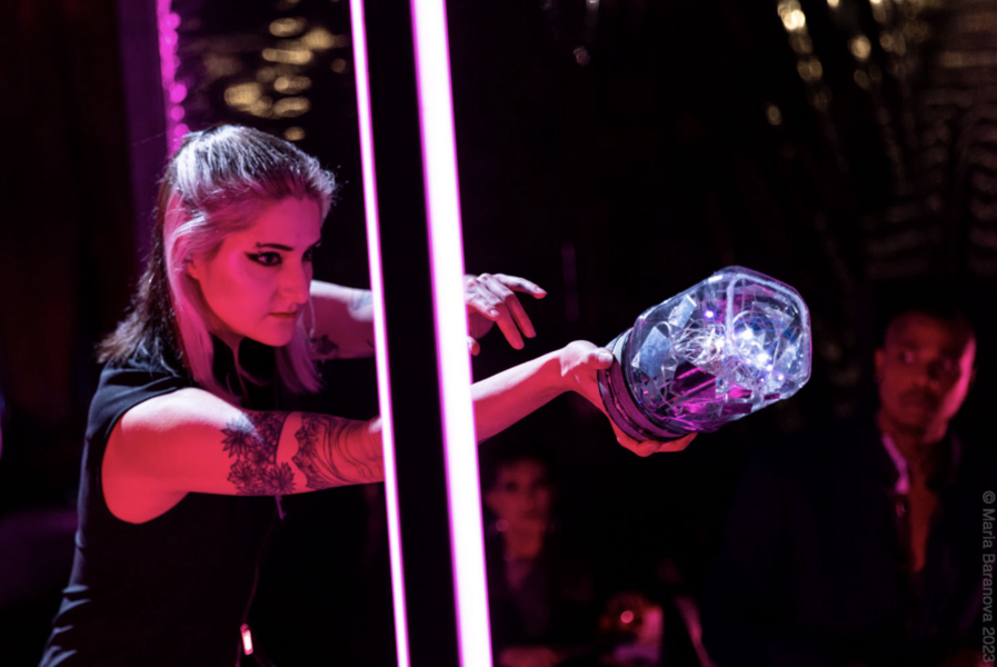 Nina Masuelli, lit in pink, thrusts forward a glowing glass container about the size of a Mason jar