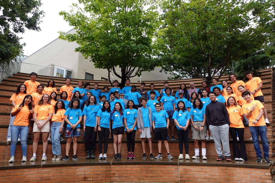 About 50 dynaMIT and MIT students wearing matching blue or orange T-shirts pose in three rows on the steps of the Stata Center