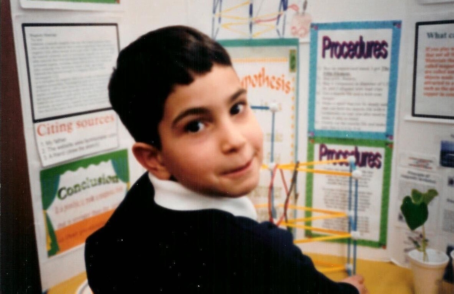 Ubadah Sabbagh as a young child smiles at camera in front of a scientific poster.