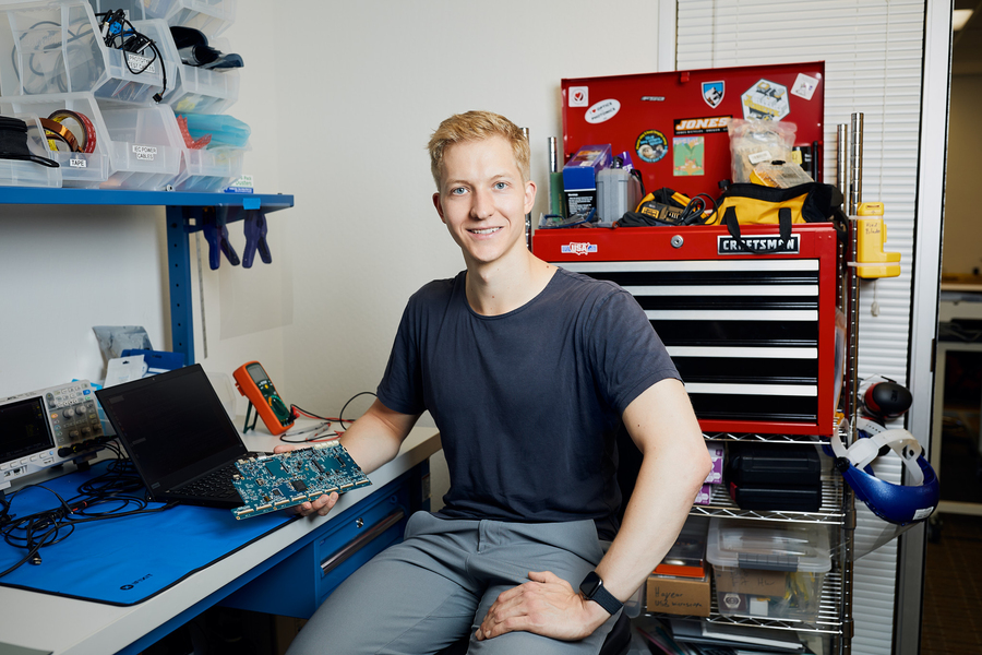 Eric Dahlseng, a young man wearing a T-shirt, sits in his lab surrounded by electrical tools and circuits.