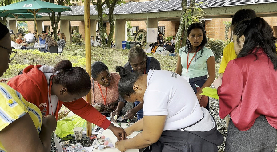 Seven women surround a small circular table, where they’re working on something together