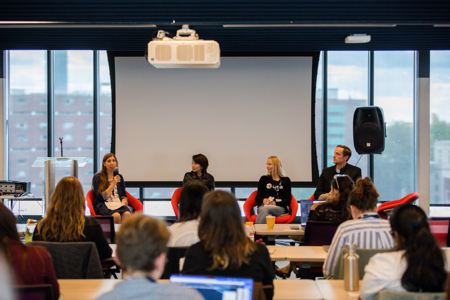 Three women and one man sit on a panel in front of an audience