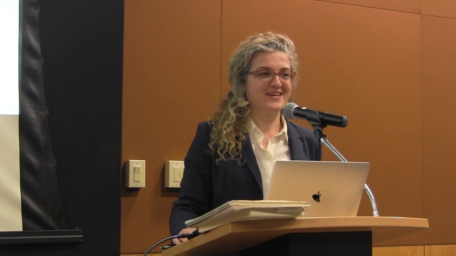 Lerna Ekmekcioglu speaks while standing at a lectern with a laptop open in front of her