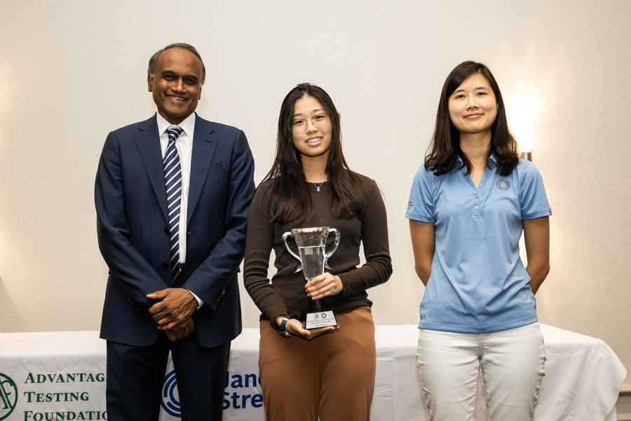 Arun Alagappan, Jessica Wan, and In Young Cho pose in front of a table in a white room. Wan holds a trophy.