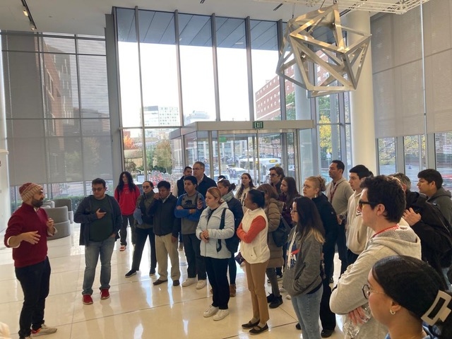 Pedro Reynolds-Cuellar addresses a couple of dozen participants in a glass atrium