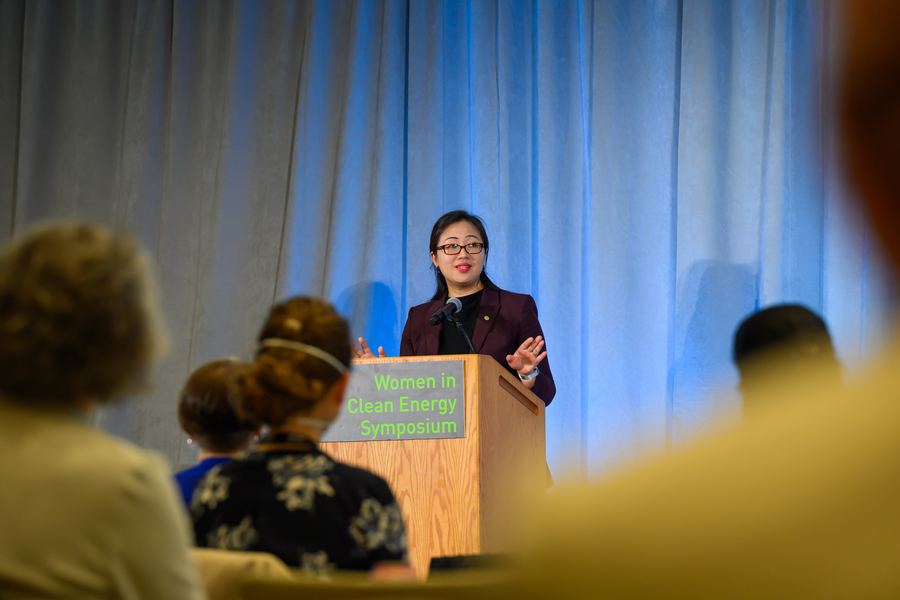 Jie Xiao stands behind a lectern with the backs of the audience in the foreground.