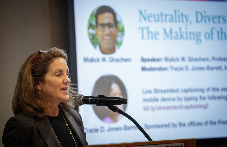 Cynthia Barnhart speaks into a microphone while a screen in background shows Malick Chachem and Tracie D. Jones-Barrett.