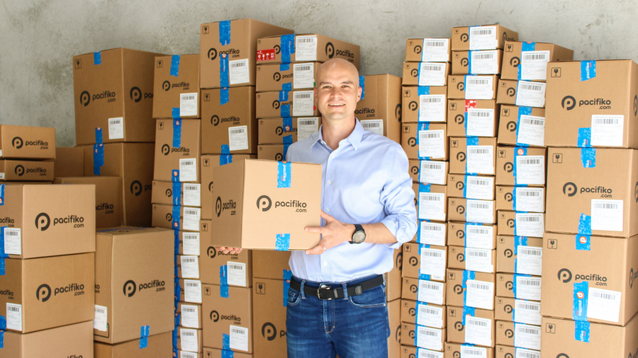 Jorge Schippers holds a cardboard box and smiles while surrounded by more boxes, all with the Pacifiko logo on them.