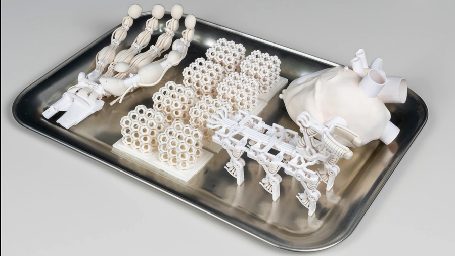 A tray contains several 3D-printed objects: a robotic hand, 8 lattice cubes, a walking robot, and a heart.