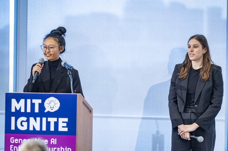 Katie Chen stands behind podium that says MIT Ignite, speaking into a microphone, while Leandra Tejedor stands next to her.