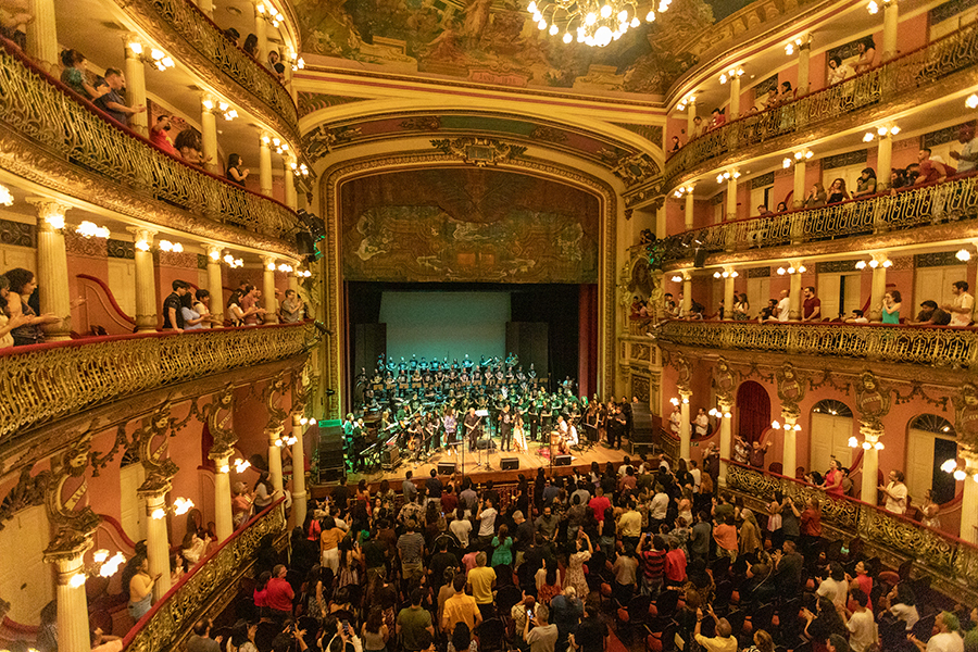 The interior of an ornate performance hall with a full audience watching musicians perform on stage