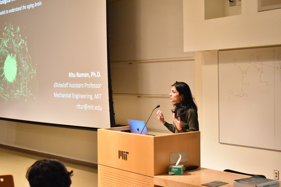 Ritu Raman stands behind a lectern, speaking into a microphone and gesturing with her hands. 
