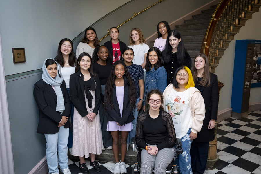 15 young women pose on the landing of a large spiral staircase