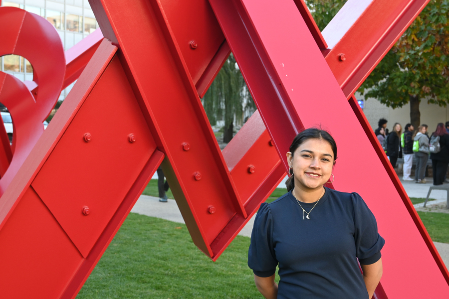 Gitanjali Rao stands in front of an outdoor sculpture comprised of red I-beams, her hands behind her back.