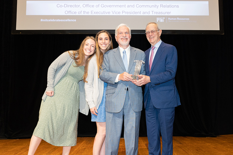 Four people stand together smiling for a photo on stage: Paul Parravano and Rafael Reif, who jointly hold a silver award, and Parravano’s daughters.