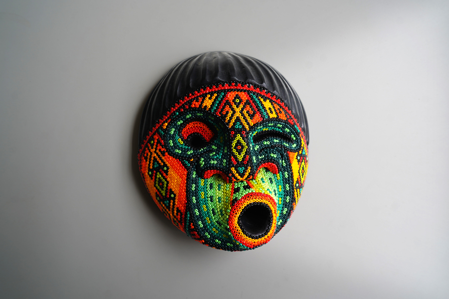 Colombian traditional mask creating a face with hundreds of colorful beads. The face is winking and has an expressive round mouth.