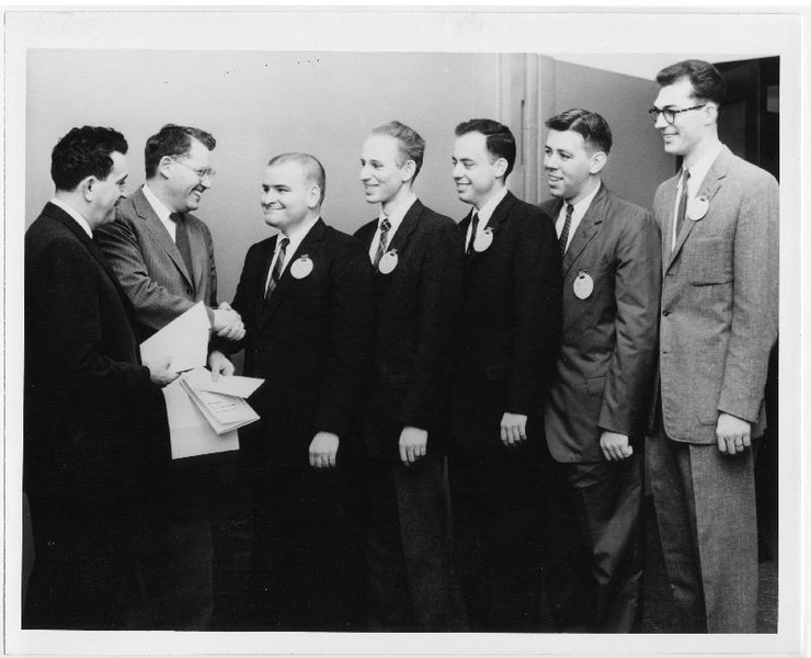 In this black-and-white photo, a young Fred Hennie stands in a line of other graduate students being given awards by the then-head of the Department of Electrical Engineering. All of the men are wearing suits and ties.