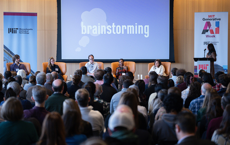 Audience watches panel of five seated individuals on stage in front of screen that reads "brainstorming"