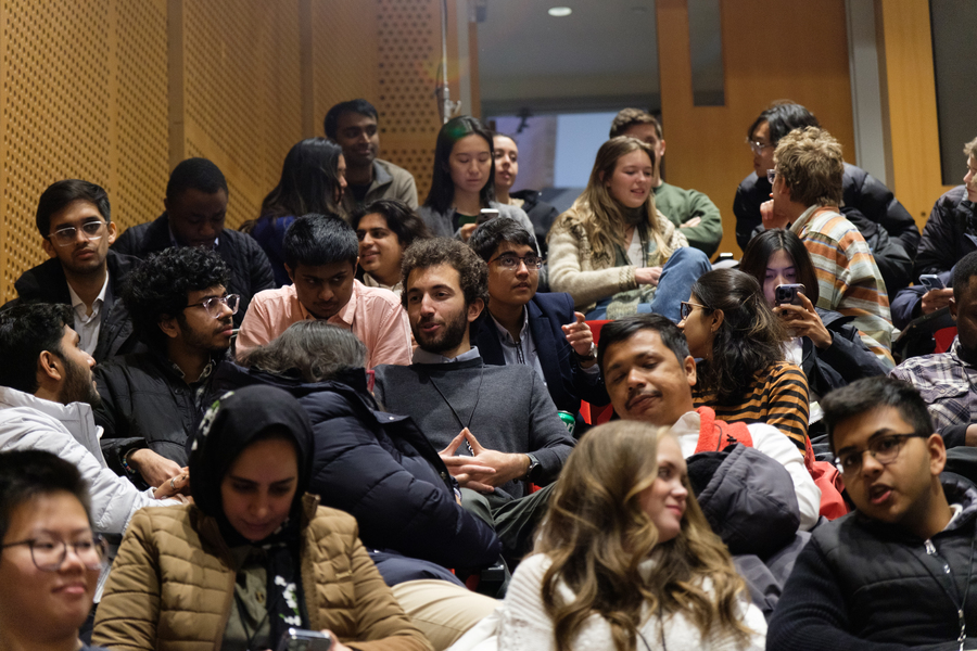Event attendees sitting in a MIT classroom, conversing or staring at their phones