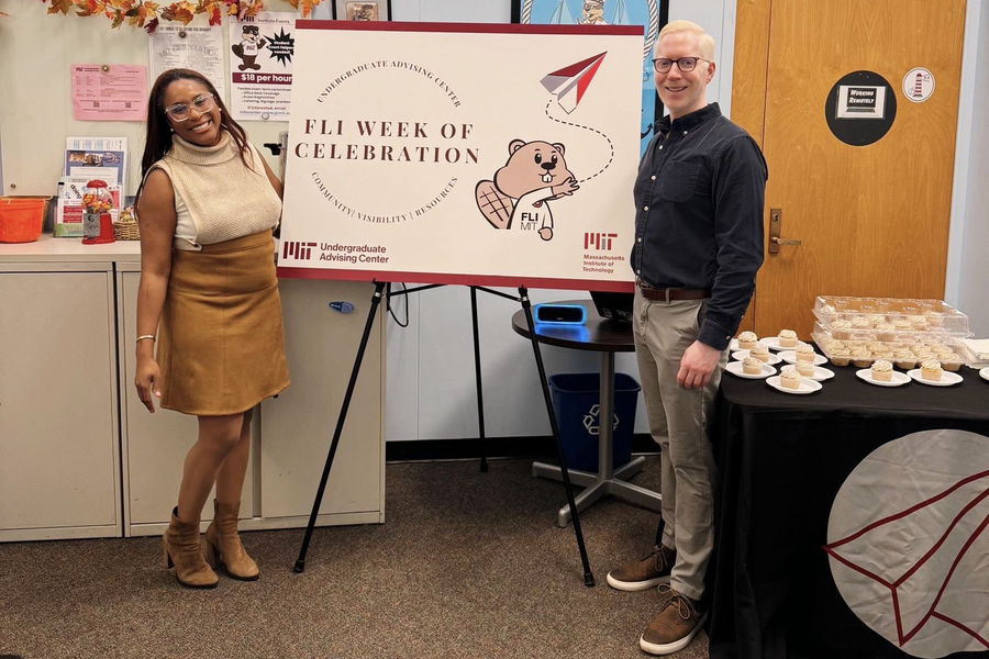 Sade Abraham and Alex Hoyt flank a poster on an easel. Behind Hoyt is a table laden with cupcakes on paper plates.