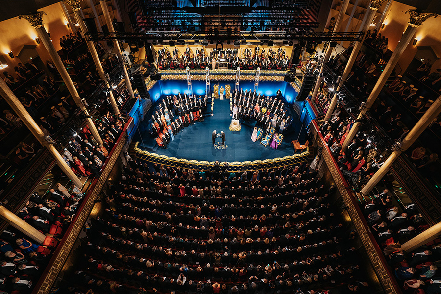 View of a large concert hall filled with audience members and many people seated on a stage for the Nobel ceremony