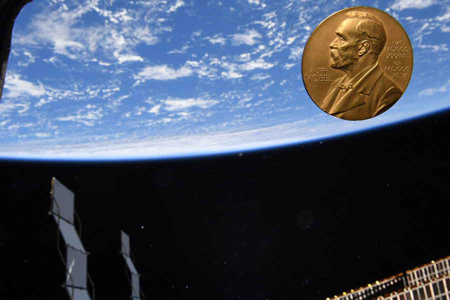 A gold Nobel Prize medal floats in the ISS cupola with other parts of the space station in view on the other side of the window, and the blue of Earth behind that.