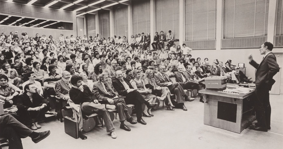 Black-and-white photo of Robert Solow speaking at a lecturn in front of a filled lecture hall
