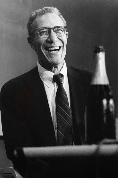 Black-and-white portrait photo of Robert Solow, laughing with a bottle of champagne in front of him