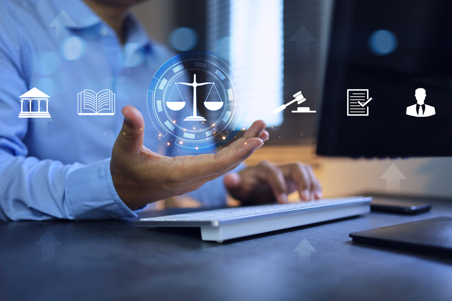 Close-up photo of a hand gesturing toward a series of floating icons resembling an ancient Greek temple, a book, a balanced scale, a gavel, a paper with a checkmark, and the silhouette of a person in a suit from the bust upwards.