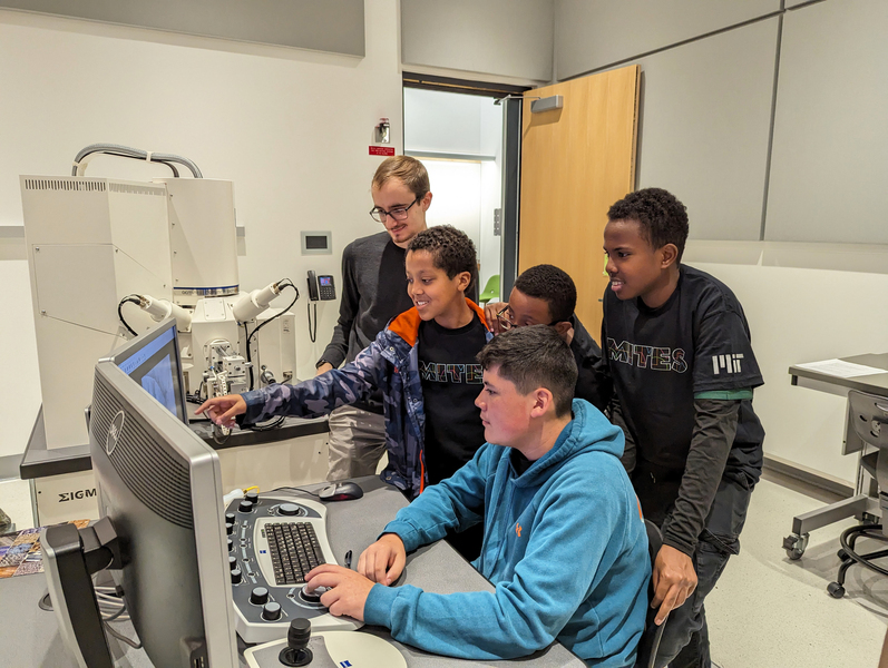 An MIT grad student helps four middle-school students use a scanning electron microscope.