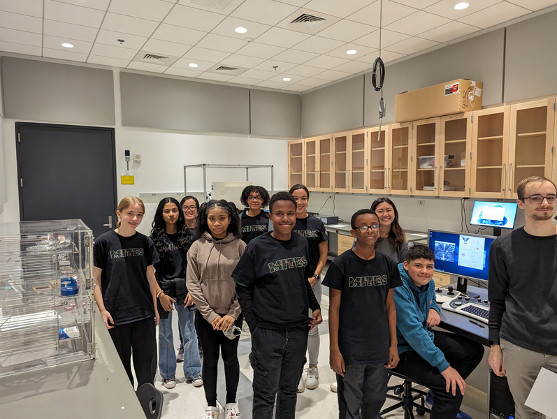 10 middle school students and one adult smile for a photo in a laboratory at MIT.