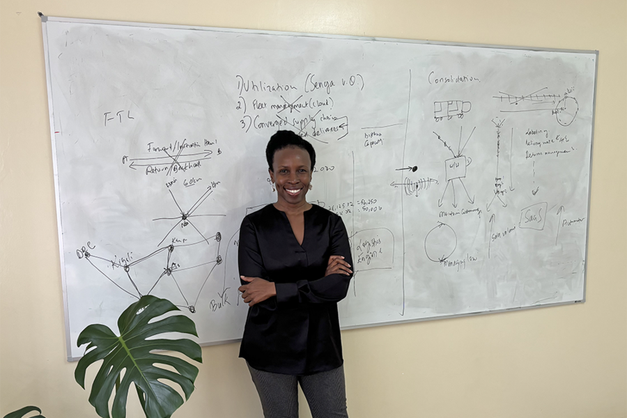 June Odongo poses in front of a whiteboard with writing on it. 