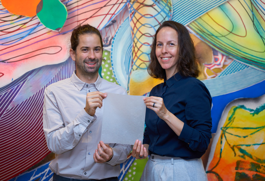 Jose Tomas Dominguez (left) and Paloma Gonzalez-Rojas stand in front of a colorful background. They're holding a square piece of translucent, paper-like material