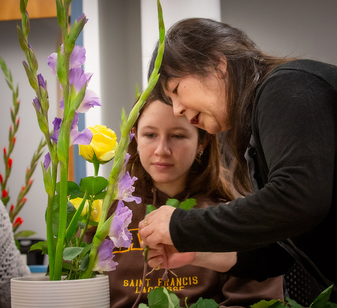 Hiroko Matsuyama works with a student to help arrange her flowers. The flowers are purple and yellow.