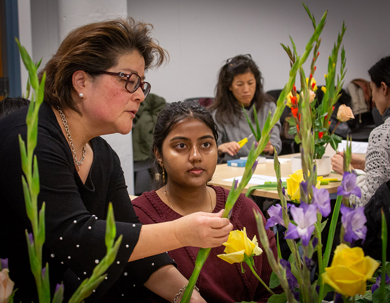 Ping Wong works with a student to help arrange her flowers. The flowers are purple and yellow.