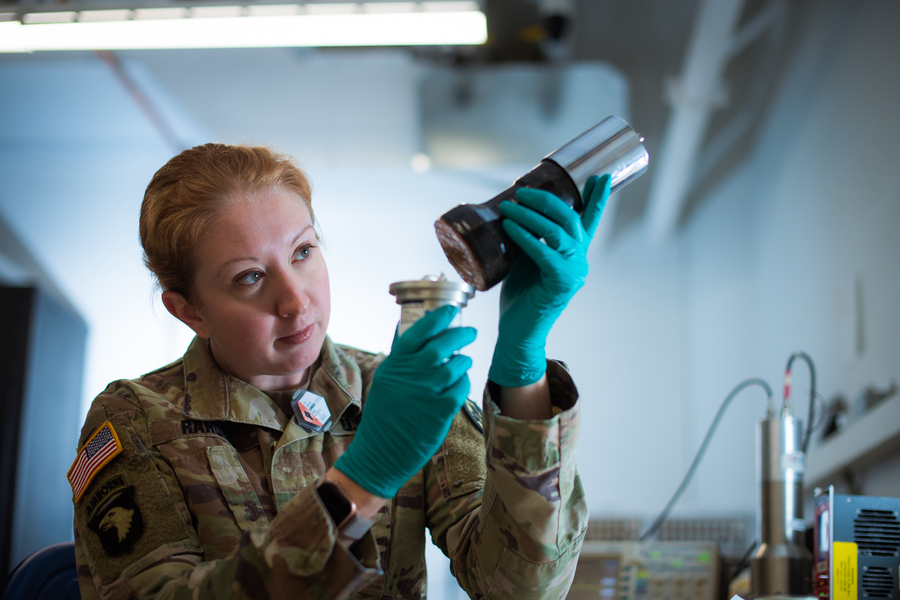 Jill Rahon in Army fatigues holding and examining instruments in a lab.