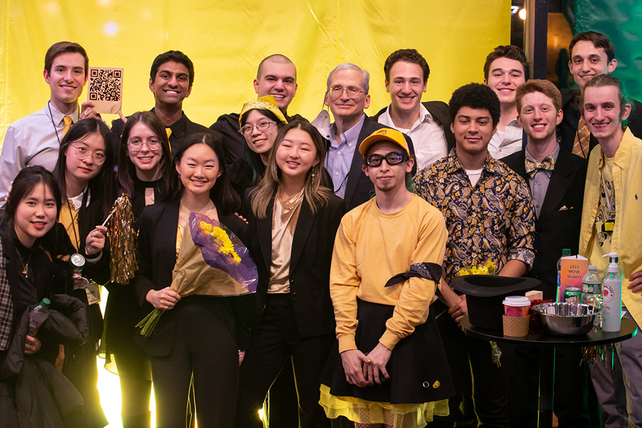 16 mechanical engineering students, mostly dressed in yellow to represent their team color, stand together against a yellow background with Richard Wiesman in the center