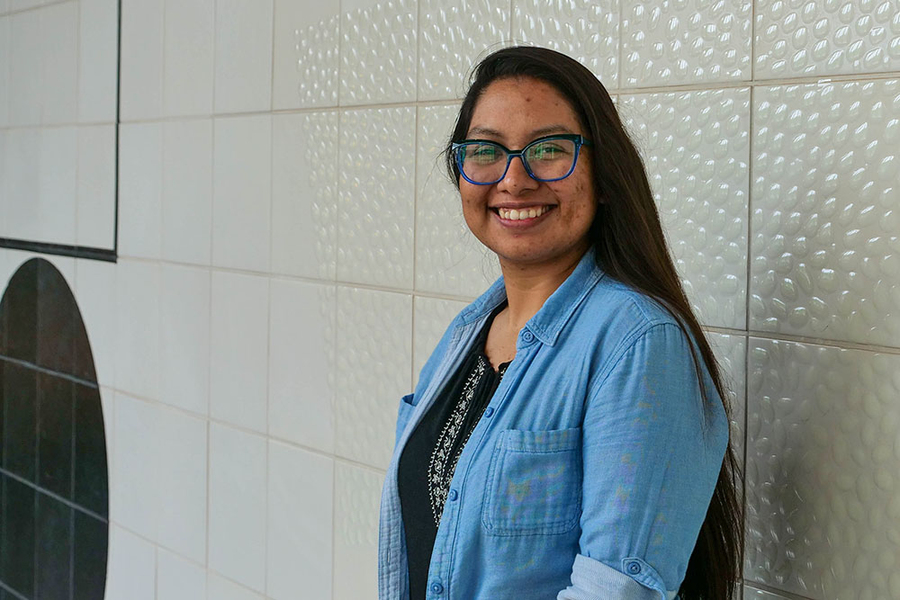 Juana De La O posing in three-quarters profile against a light gray tile wall